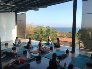 A group of people performing yoga on a rooftop deck overlooking beautiful scenery